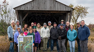 a group of people stand outside a barn on a fall day