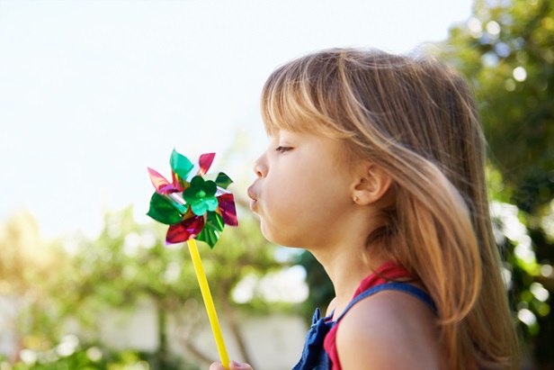child blowing at wind spinner