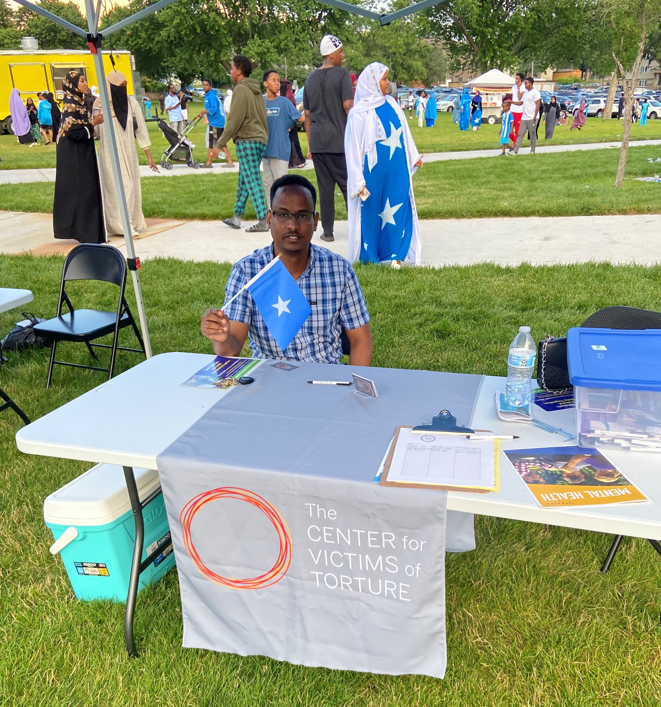 Man sitting at Center for Victims of Torture display table at outdoor community event