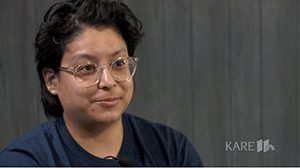 a woman with short black hair and clear glasses wearing a navy teeshirt.