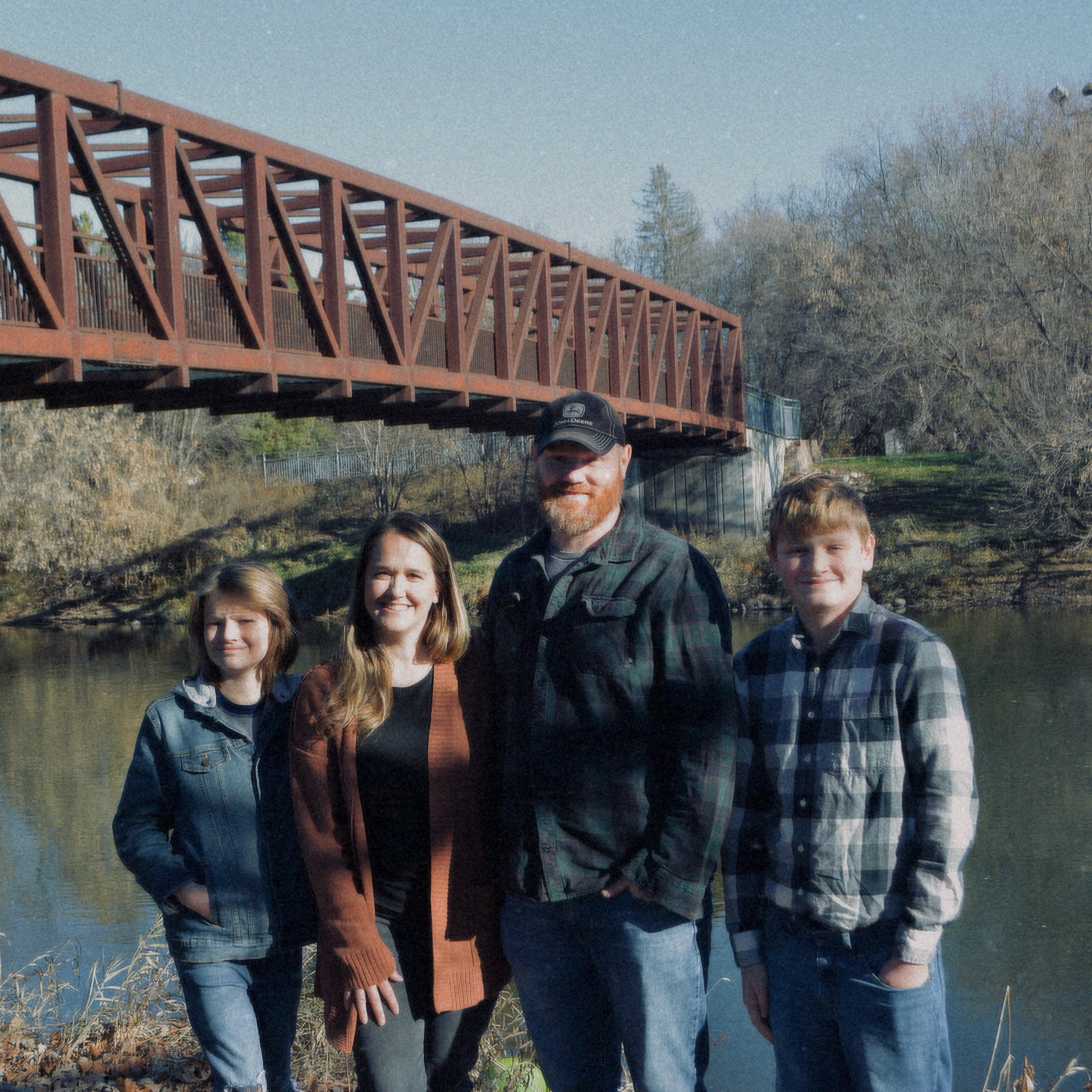 family stands next to a bridge on a fall day.