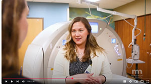 A woman with blond hair stands in front of an MRI machine