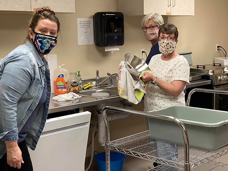 Three people wearing masks and washing dishes in church kitchen